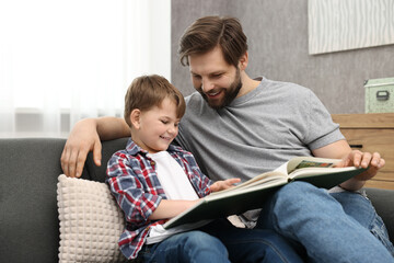 Happy dad and son reading book together on sofa at home