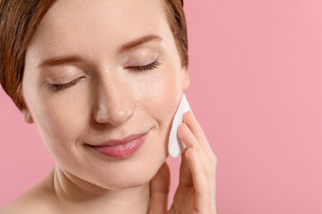 Beautiful woman with freckles wiping face on pink background, closeup. Space for text