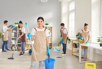 Cheerful woman, part of the cleaning team, stands with a mop and bucket, bringing a positive vibe...