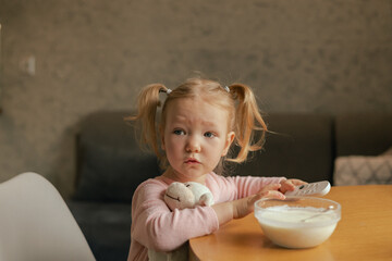 Baby girl eats breakfast and switching channels on the TV with the remote control. Harmful...