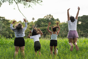 four latin girls jumping and raising their hands in a field of tall grass, park or nature reserve