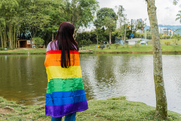joven mujer de espaldas con la bandera del orgullo gay cubriendo su cuerpo al aire libre 