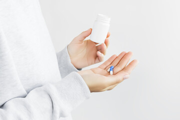 woman holding two blue and white medicine capsules on her palm and empty white plastic jar