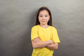 portrait of an Asian girl in a yellow T-shirt with long hair on a gray background, copy space,...