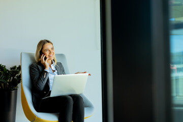 Businesswoman in modern office talking on phone and using laptop during daytime