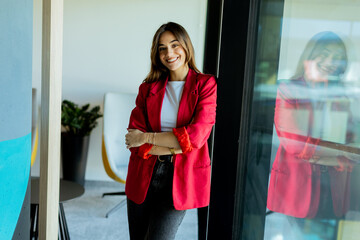 Confident young professional in red blazer smiling at modern office environment