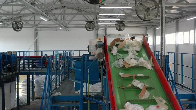 A lot of factory workers sorting the waste material coming from a conveyor. Multiple factory workers separating the trash from a conveyor belt. Factory workers categorising the rubbish from a conveyor