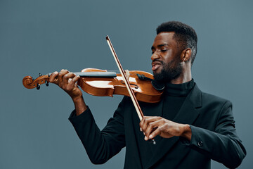 Talented African American man playing violin with passion and skill on gray background in studio...