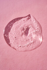 Drop of serum shimmering in the sun on a pink background.