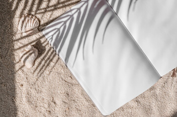 Open notebook with blank sheets mockup on neutral beige beach sand texture background with tropical palm tree sunlight shadows, luxury resort vacation and relax concept