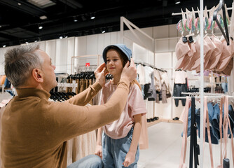Father Helping Daughter Try On Hats In Modern Clothing Store On Weekend