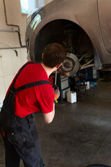 a mechanic stands by a car in a car service center. master repairs car brake discs and pads