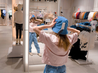 Young Woman Trying On Blue Hat in Modern Clothing Store in Afternoon