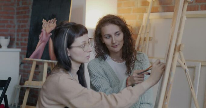Young woman drawing and talking to art teacher enjoying individual lesson in creative studio. Visual arts and master class in workshop concept.