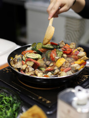chef cooking in a vegetable casserole with a wooden spoon