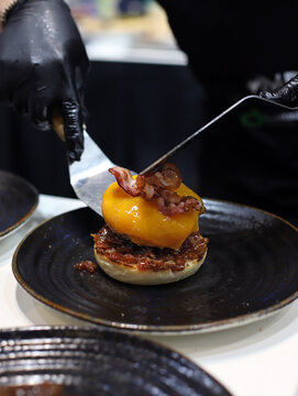 chef sirviendo una hamburguesa de carne, queso fundido y beicon en un plato con paletas de cocina