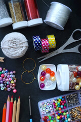 Colorful beads, coloring pencils, glitter, needles, string, hoop, tape and scissors on dark...