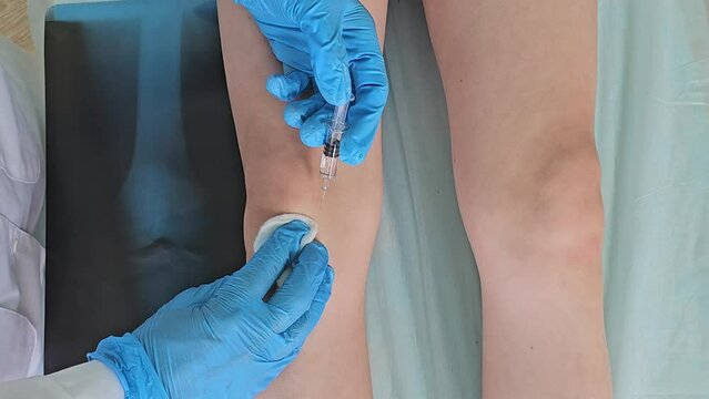 Doctor gives an injection to a patient, a child teenager, in a clinic, close-up. Treatment for knee problems