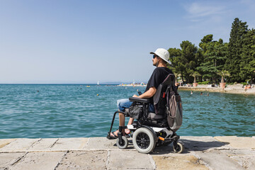 Tourist man with a disability sitting on the dock and looking at the open sea. Wheelchair travel...