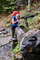 A woman hiker drinking from a fountain on a trail.