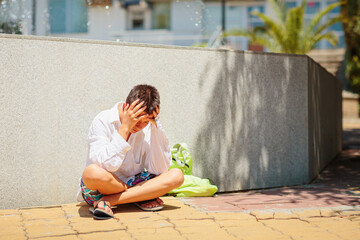Sad depressed teenager sitting upset near the fountain and holding his head in his hands. The idea...