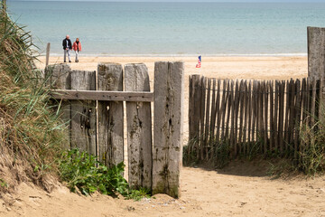 Utah Beach in Normandy, Two unrecognizable people. USA Flag on wood sea fence, Grass and sand....