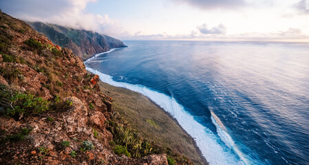 View of rough ocean with waves, volcanic beach, sunset over a huge cliff  in Lighthouse Ponta do Pargo, Madeira, Portugal