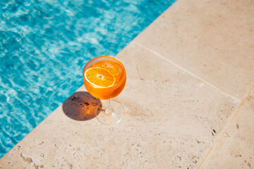 Glass of spritz aperol with orange slice against poolside at resort hotel during vacation.