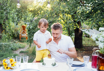 Young dad and toddler son look at sweet birthday cake outdoors. A man and a child are tasting a...