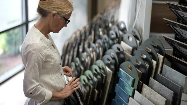 Happy mature woman looking at samples of floor tiles in a store for a home renovation redecorating project in a flooring store.