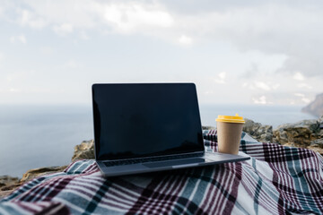 Laptop coffee on blanket with ocean view. Illustrating serene outdoor laptop use. Freelancer...