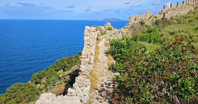 The Old Navarino castle (Palaiokastro, Paliokastro), ruined defense walls with battlements overgrown with green grass and bushes, seascape in the background, Greece.
