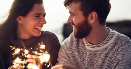 Happy, couple and fireworks sparkle at celebration with happiness on holiday or vacation in summer....