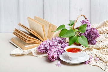Porcelain cup with tea, vintage book and lilacs in the background.