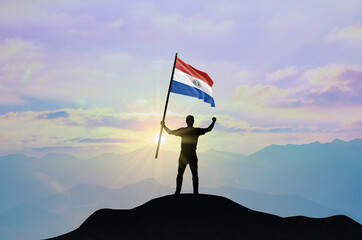 Paraguay flag being waved by a man celebrating success at the top of a mountain against sunset or sunrise. Paraguay flag for Independence Day.