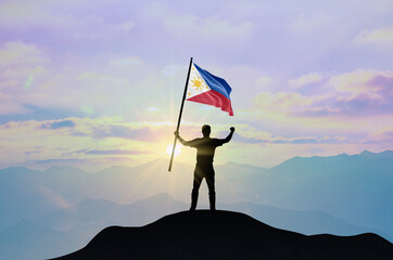Philippines flag being waved by a man celebrating success at the top of a mountain against sunset or sunrise. Philippines flag for Independence Day.