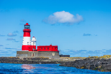 Longstone Lighthouse in the Outer Farne Islands on the Northumberland Coast, UK, with basking seal and seabirds on lichen covered rocks.  Horizontal.  Space for copy.