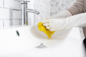 Close-up shot of woman in rubber gloves cleans sink and faucet with a rag and spray in the...