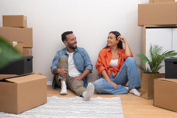 Married couple enjoys moving in new spacious apartment in another city together sitting with...