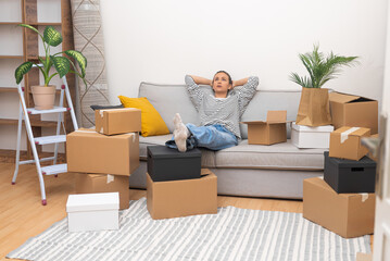 Woman sits on soft sofa waiting for help of husband in collecting boxes with furniture standing...