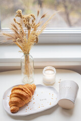 White glass and a plate on which lies a croissant made of clay with the inscription love, handmade.