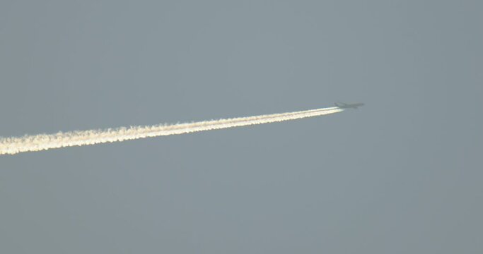 The flight of a dark plane through the pale blue sky from left to right up. Immersion trace in the background light.