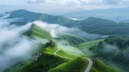 A breathtaking view of a mountain landscape with a road cutting through green valleys, misty fog, and floating clouds