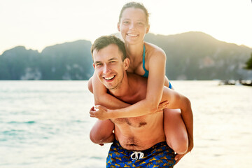 Portrait, piggy back and beach with couple, vacation or happiness with sunshine, getaway trip or...
