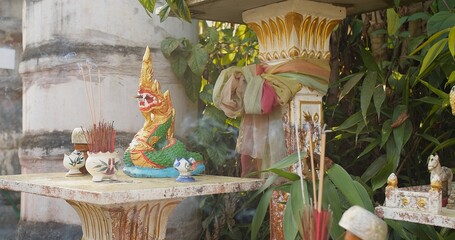 A table with a statue of a dragon snake naga and a bunch of incense sticks. thai traditional...