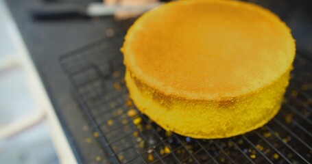A yellow cake on a cooling rack. The cake is golden brown and has a slightly burnt edge. The cake is placed on a black countertop