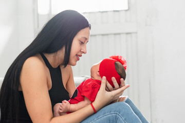 young latina mother looking proudly at her beautiful newborn baby girl while carrying her on her lap