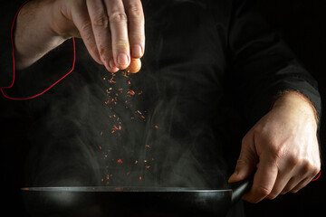 A professional chef adds aromatic spices to a hot, steaming frying pan. The concept of preparing a...