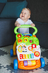 A blue-eyed baby learns to walk with the help of a walker. The baby is developing and learning to...