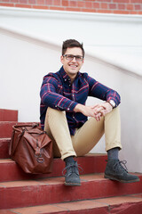 Man, sitting and steps in portrait with glasses for career, financial advisor or economist with smile. Male accountant, fashion and staircase with travel bag for job, investing in New York for future